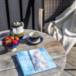 Round table with tea, strawberries, and book on terrace.