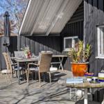 Deck with table, chairs, plants, and fire pit beside dark wooden house.