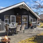 Deck with seating, grill, and closed umbrella in front of a wooden house.