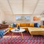Living room with yellow sofa, wooden ceiling, and wood stove.