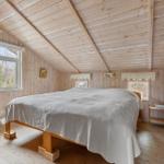 Bedroom with wooden walls and ceiling, large bed, windows, and heater.
