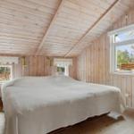 Bedroom with wooden walls and ceiling, large bed, windows overlooking garden.
