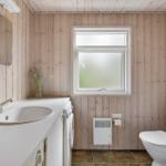 Bathroom with wooden walls, sink, toilet, and window.