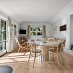 Dining area with round table, chairs, and stove. Kitchen with green cabinets and windows.
