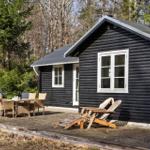 Black log cabin with deck, lounge chairs, and grill. Surrounded by forest.