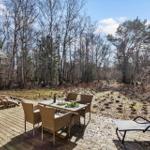 Deck with table, chairs, and grill. Background: forest with trees.