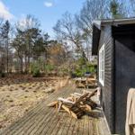 Wooden terrace with lounge chairs and shower next to a dark wooden house in the woods.
