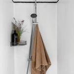 Shower stall with overhead and handheld showerheads. Towel hanging. Shelf holds bottle and dried flowers.