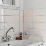 Sink with faucet and care items on white tiled wall