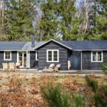 Black wooden house with terrace, garden, and forest in the background.