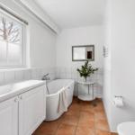 Bathroom with bathtub, sink, and toilet. Window, mirror, and plant visible.