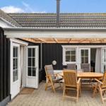 Terrace with wooden table and chairs, white doors, and black wooden house with roof.