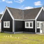 Black wooden house with white window frames and door, grassy area in front, clear sky.
