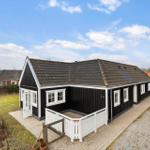 Black wooden house with white railing and tiled roof. Garden and path are visible.