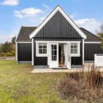 Black wooden house with white trim and open entrance. Lawn and trees in the background.