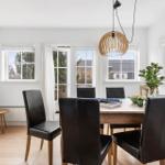 Dining room with wooden table, black chairs, and large windows.