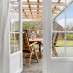 Through the glass door, a paved outdoor area with a wooden table, chairs, and a bottle is visible.