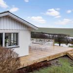 House with terrace, table, and chairs. View of fields and sky.