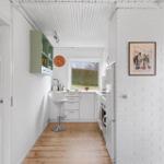 Kitchen with white cabinetry, wooden floor, and window. Left bedroom, right hallway.