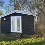 Black wooden cabin with white door and roof edge in the woods.