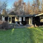 A dark wooden house with a terrace and garden. Multiple windows and doors are visible.