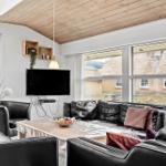 Wohnzimmer mit Ledersofa, Fernseher und großen Fenstern.