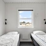 Zwei Betten mit weißen Bettwäschen, Fenster mit Blick auf Außengelände, weiße Holzwandverkleidung.