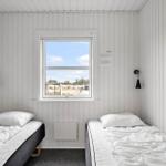 Zwei Einzelbetten mit weißen Bettwäsche, Fenster mit Blick nach draußen, weiße Holzwände.