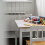 Tisch mit Stühlen und Kinderspielen in einem Raum mit weißer Wandverkleidung.