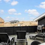 Terrasse mit Liegestühlen und Grill, Blick auf Dünenschutzwälle und Häuser.