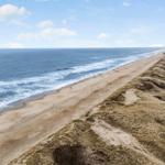 Strand mit Dünen und Meer unter blauem Himmel