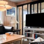 Wohnzimmer mit Sofa, Fernseher und Holztisch. Große Fenster und Holzwände.