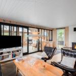 Wohnzimmer mit Kamin, Fernseher und Sitzgelegenheiten. Große Glasfront zur Terrasse.