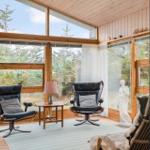 Zimmer mit zwei schwarzen Sesseln, Tisch und Blick auf Wald durch große Fenster.