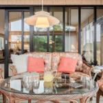 Wohnbereich mit Sofa, Sesseln und Glas-Tisch. Große Fenster und Holzwände.