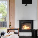 Kamin mit brennendem Feuer, Holzwände und Fensterblick auf Bäume.
