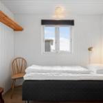 Schlafzimmer mit Bett, Stuhl und Fenster. Wände sind weiß verkleidet.