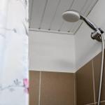 Duschkopf an der Wand, braune Fliesen und weiße Decke mit Holzverkleidung.
