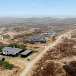 Aerial view of scattered houses on dunes near the sea.