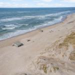 Strand mit Dünen und Wellen, einige Besucher und Betonstrukturen