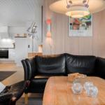 Wohnzimmer mit Ledersofa, Holztisch und Küchenbereich im Hintergrund.
