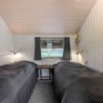 Zwei Betten mit dunklen Bettdecken stehen gegenüber einem Fenster mit grauen Vorhängen.