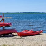 Rote Kanus liegen am Strand eines Sees unter blauem Himmel.