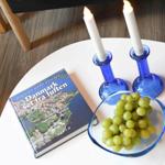 Runde Tisch mit Buch, zwei Kerzenhaltern und einer Schale Trauben.