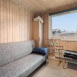 A room with sofa, chair, and wardrobe. Wooden walls and a window with view outside.