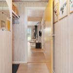 Hallway with wooden walls and view into living area with fireplace and chair.