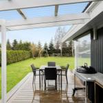 Deck with table, chairs, and grill under pergola. Lawn and play equipment in background.