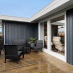 Deck with dark outdoor furniture and glass railing. View into the interior of the house.