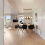 Dining area with table and chairs, living area with armchair and TV, wooden floor and white walls.