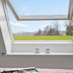 Durch das Fenster blickt man auf ein grünes Feld und einen blauen Himmel mit weißen Wolken.